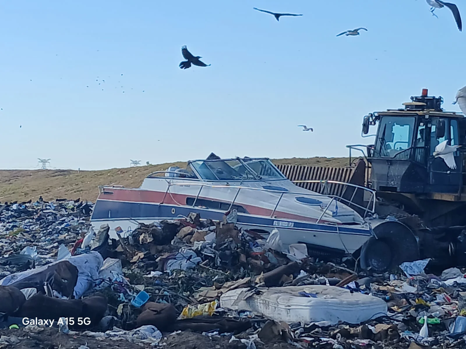 Boat hull beside heavy equipment at a disposal site