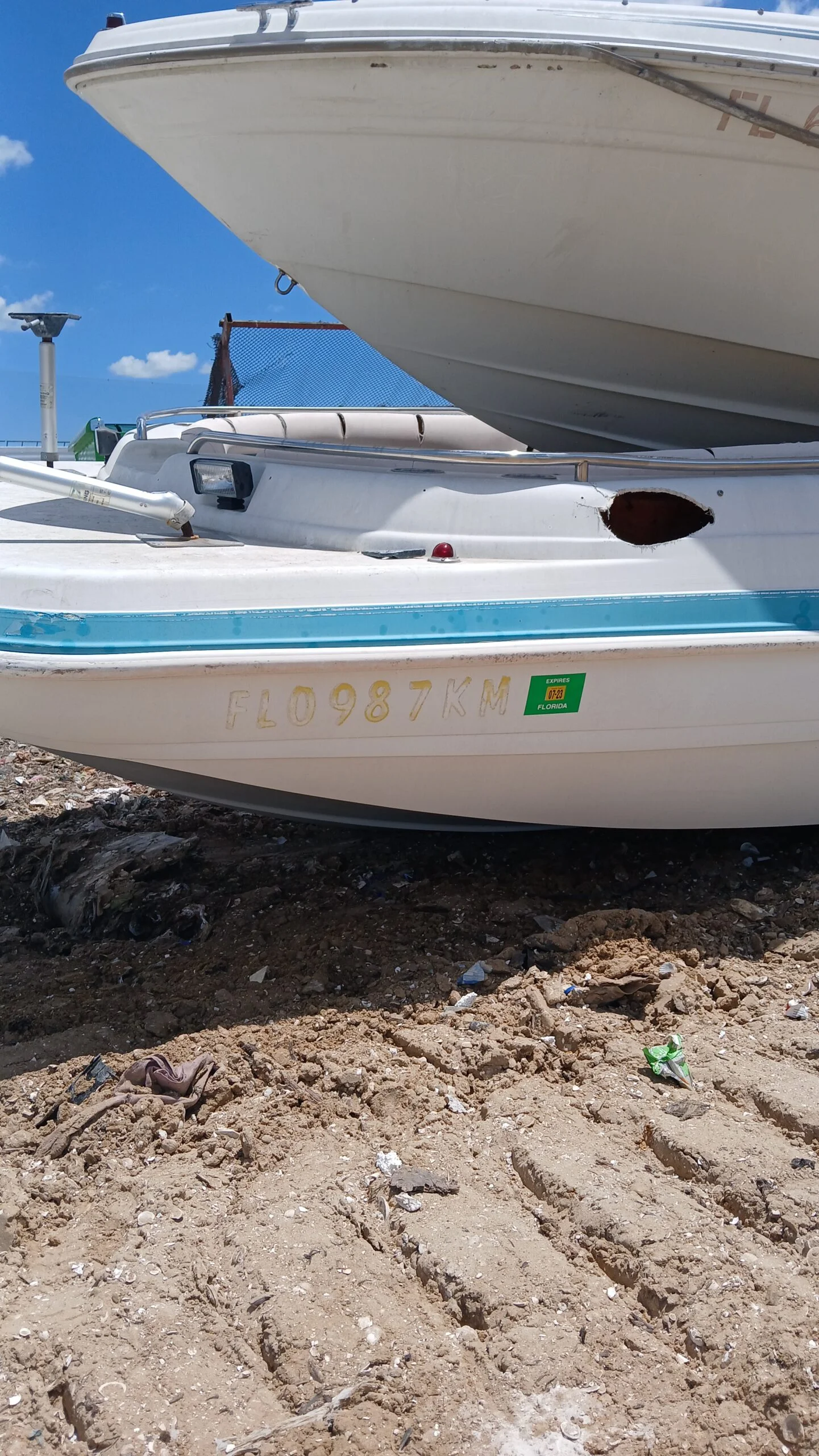 Damaged small hull beneath a larger vessel in a yard
