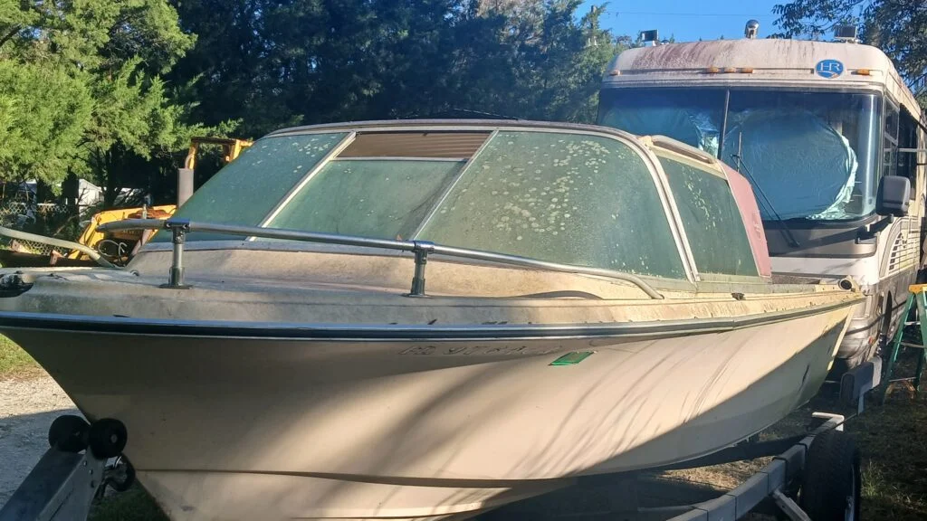 Weathered motorboat on a trailer beside a parked recreational vehicle