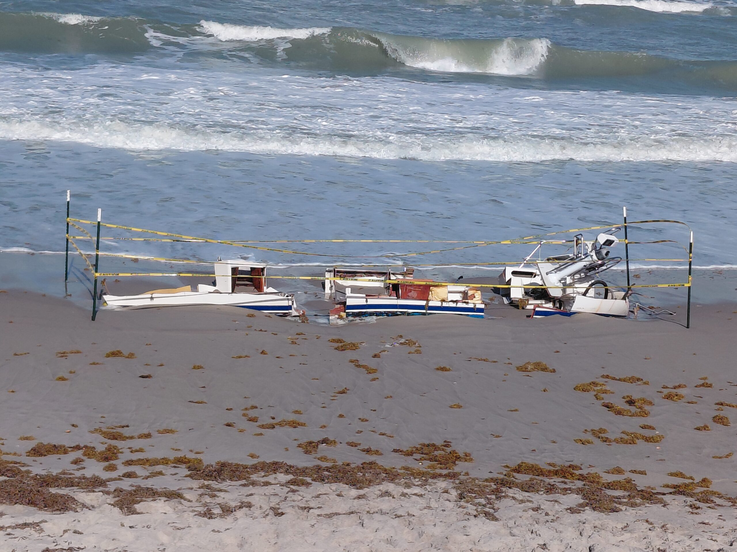 Broken vessel sections on a beach enclosed by caution tape