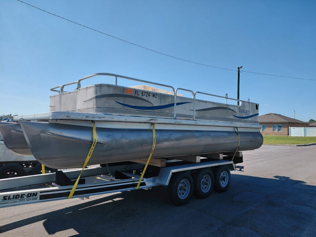 Pontoon boat strapped to a triple-axle trailer on a paved road