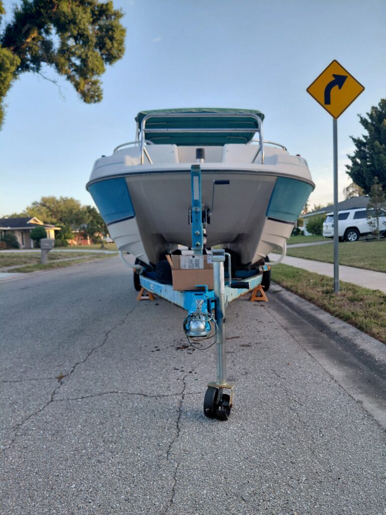 Front view of a blue and white boat resting on a trailer by a curb