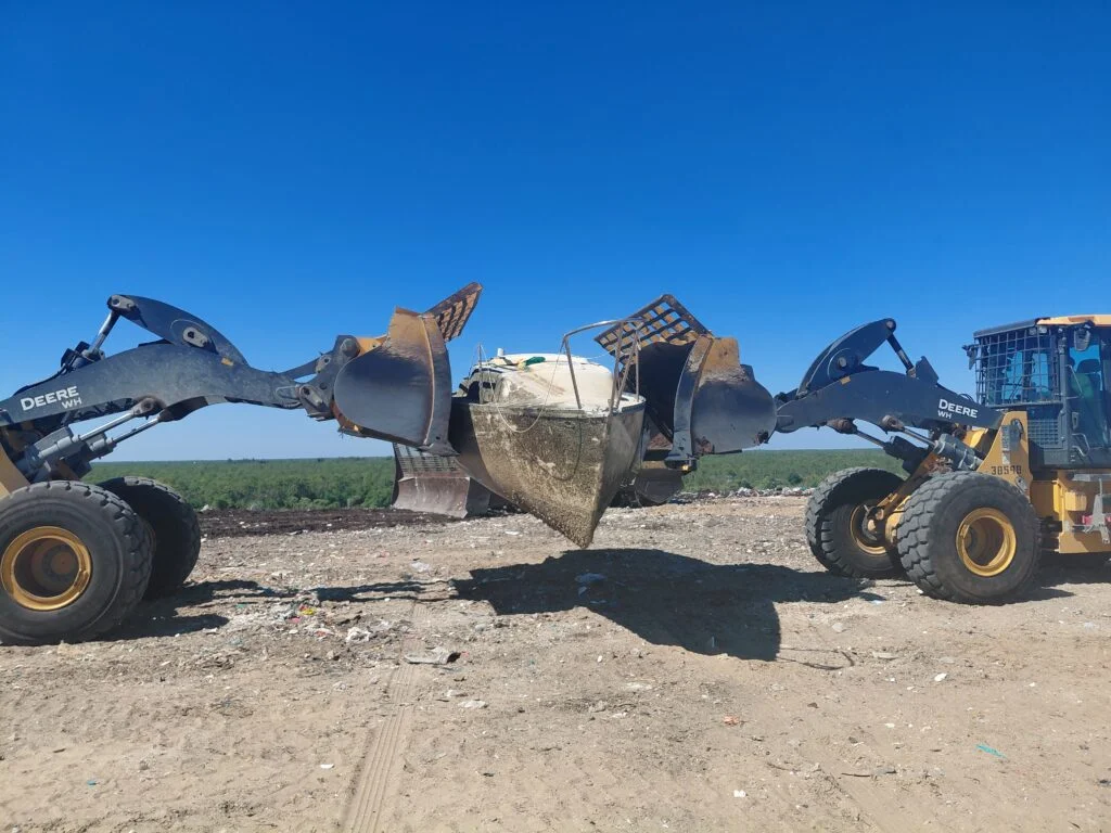 Boat hull supported between two wheel loaders at an outdoor work site