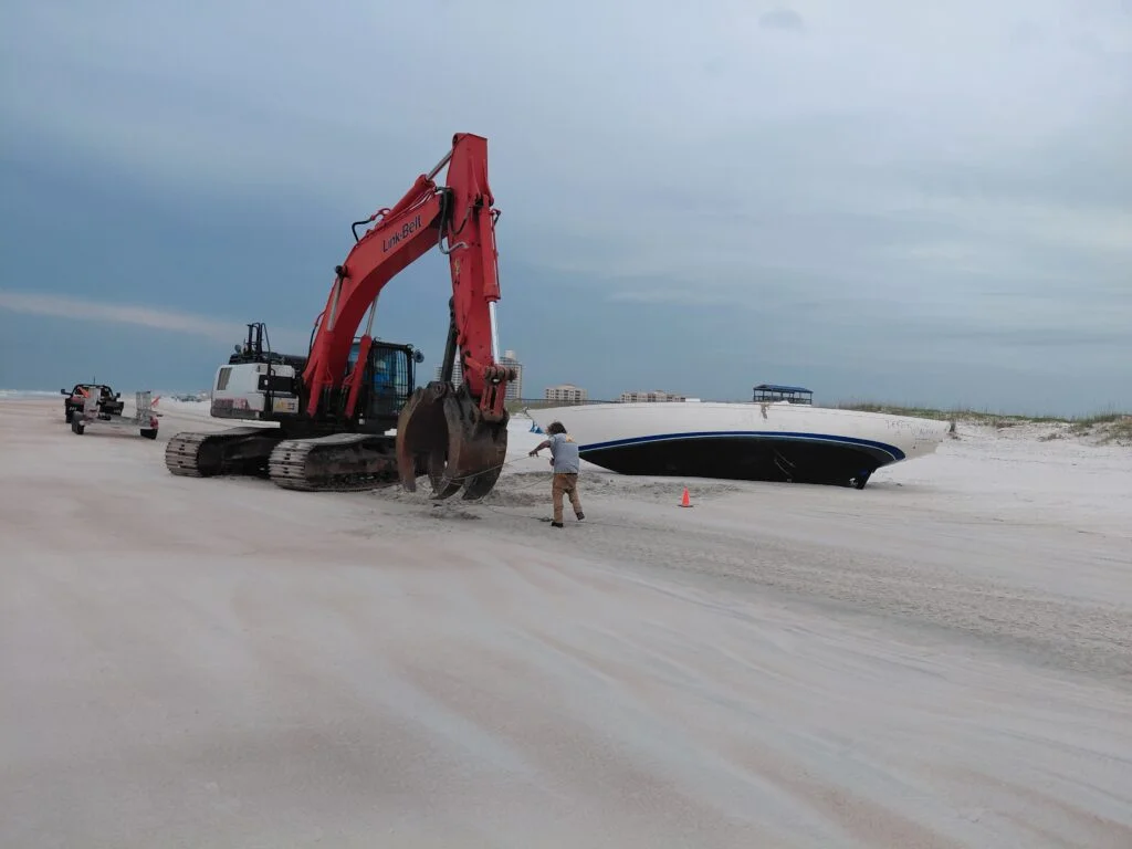 Excavator and crew beside a grounded boat on sand