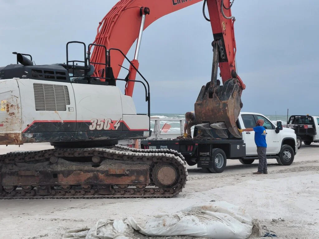 Excavator and work trucks on a beach during vessel removal work