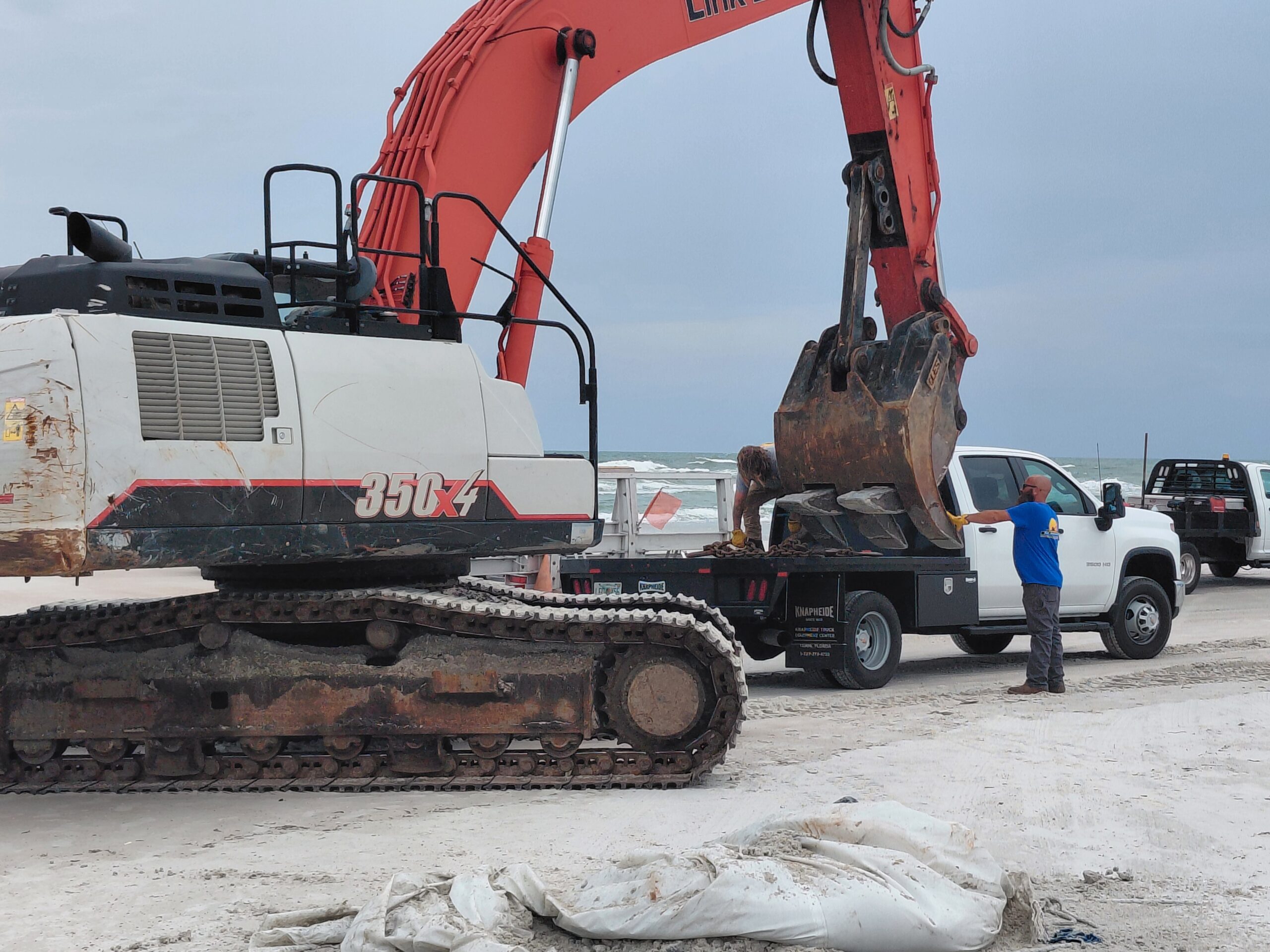 Excavator and work trucks on a beach during vessel removal work